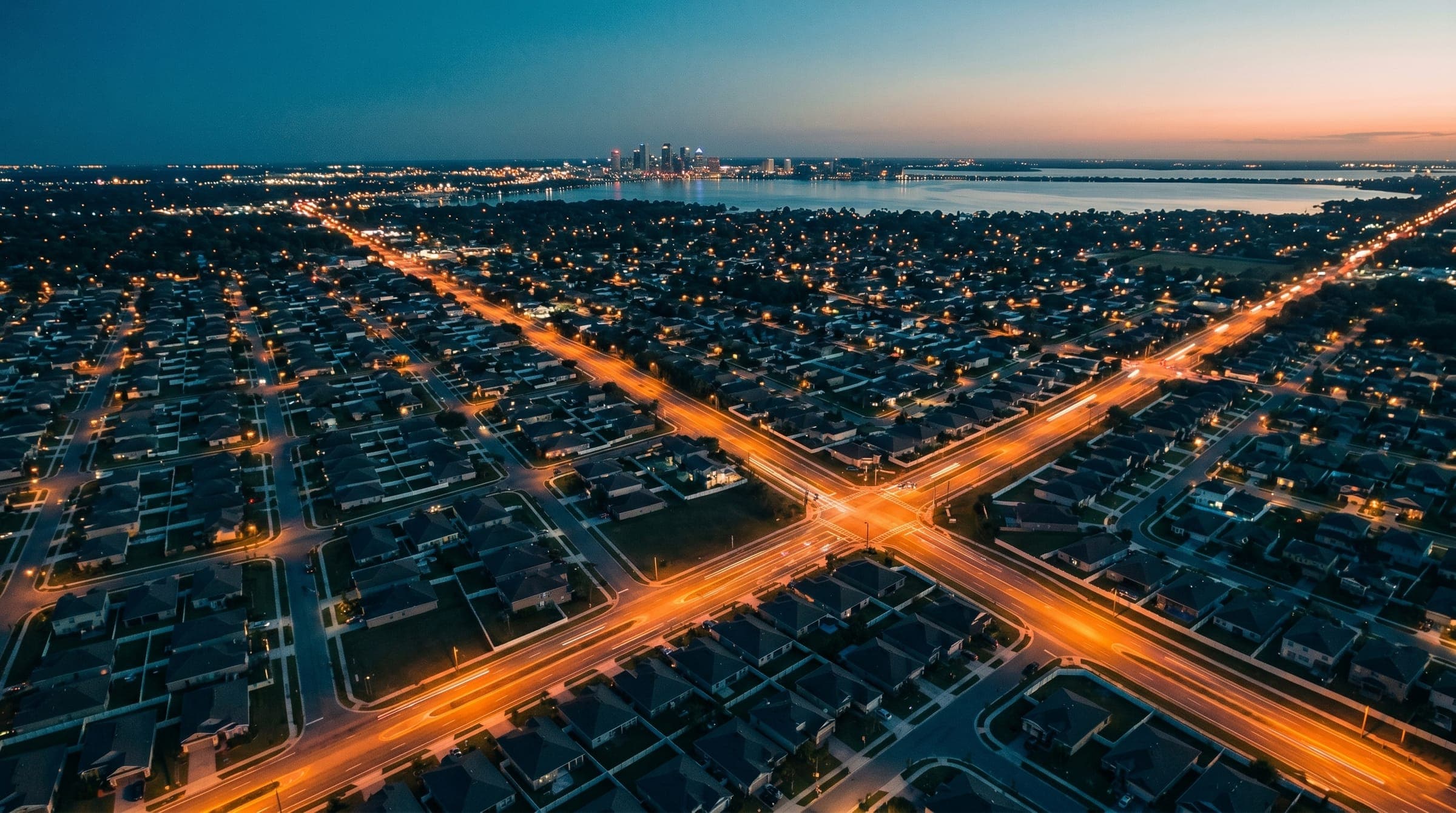 Tampa Bay from the air at dusk, suburban roads glowing orange across the metro toward the bay and skyline